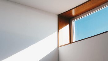 Sonnenlicht strömt durch ein Fenster und erzeugt eine scharfe Lichtkante auf einer weißen Wand, die für einen starken Kontrast in einem minimalistischen Raum sorgt.