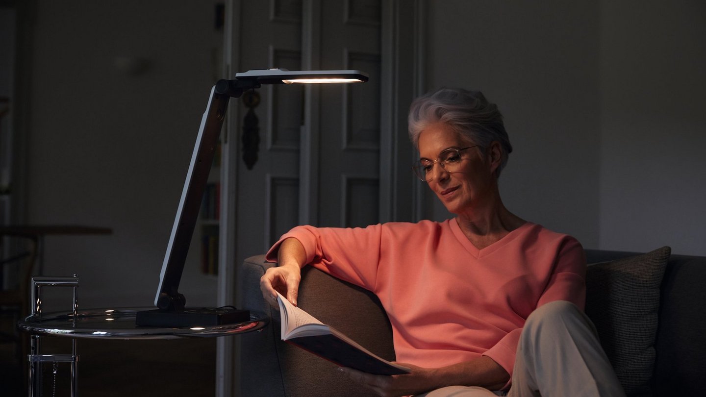 Das Foto zeigt eine lesende Frau mit der Tischleuchte elumentis LED von Eschenbach Optik.