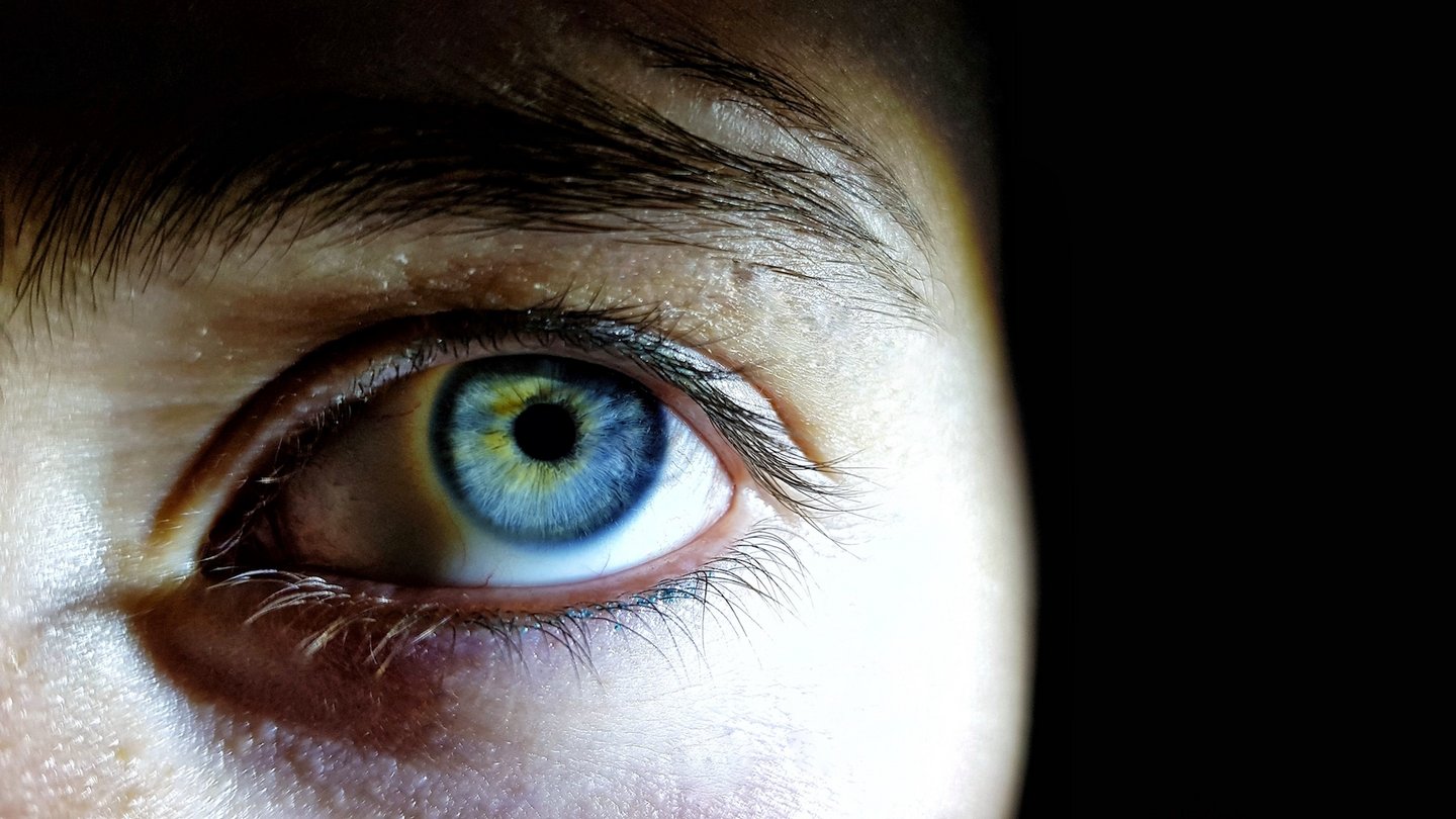 Das Bild zeigt ein blaues Auge vor einem dunklen Hintergrund.